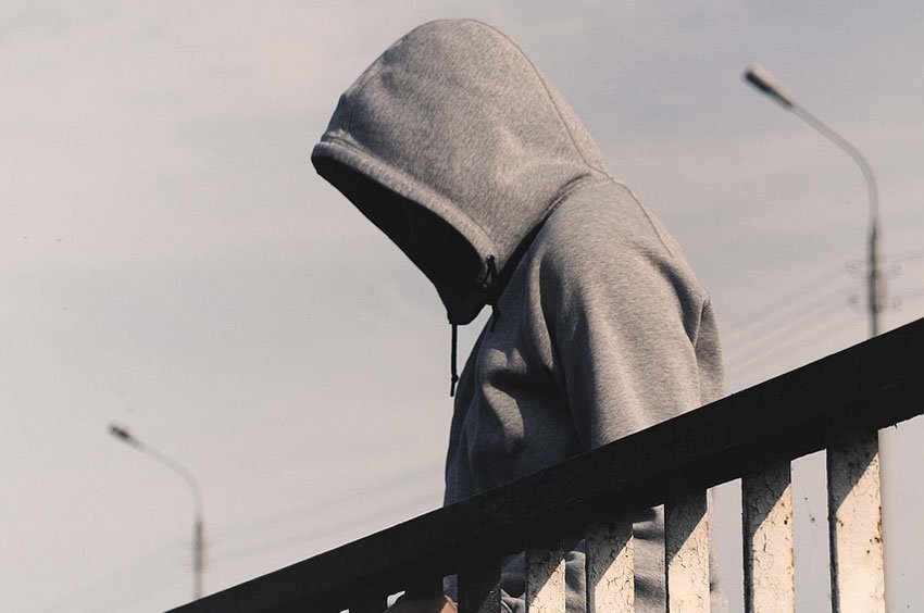 A person wearing a hoodie standing on a bridge.